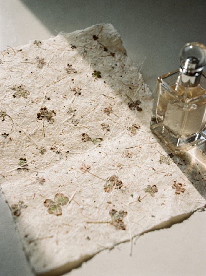 Handmade paper embedded with pressed clover beside a clear glass fragrance bottle